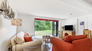 A modern living room with a sofa, a red armchair, a television, and a view of the outdoors. - Ramblers, Marnhull, Shaftesbury (Marnhull)