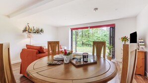 A dining area with a round wooden table, a red sofa, and a window with a red blind. - Ramblers, Marnhull, Shaftesbury (Marnhull)