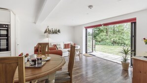 A modern kitchen with a built-in oven, a dining table with chairs, and a view of a garden through large sliding glass doors. - Ramblers, Marnhull, Shaftesbury (Marnhull)