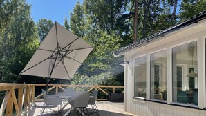 Een houten terras met een tafel en stoelen onder een grote parasol, met uitzicht op een bebost gebied.