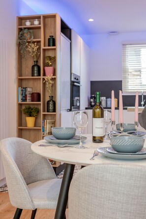 A dining area with a round table set for four, surrounded by light grey upholstered chairs. A wooden bookshelf with various decorative items is visible in the background. - Beautiful 2 bedrooms split level Fulham Apartment (London)
