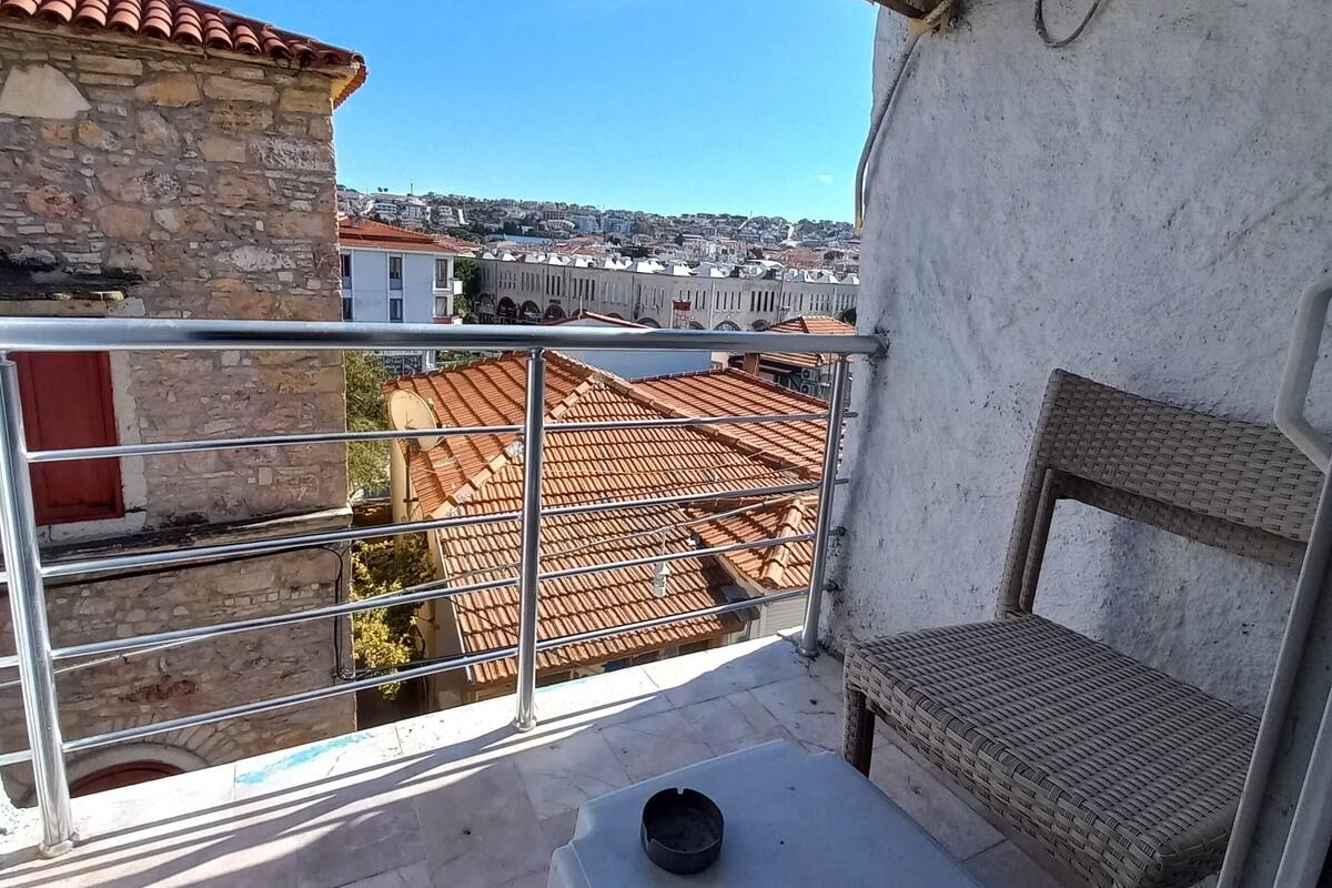 A balcony with a view of a cityscape, a wicker chair, a small table, and an air conditioning unit.