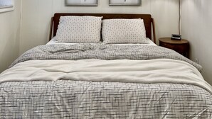 Ein Schlafzimmer mit einem Bett, zwei Pflanzenbildern an der Wand, einem Deckenventilator und einer Hängelampe.