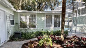 Ein Haus mit überdachter Terrasse, einem eingezäunten Garten mit verschiedenen Pflanzen und einem Pool, der durch die Glasverkleidung sichtbar ist.