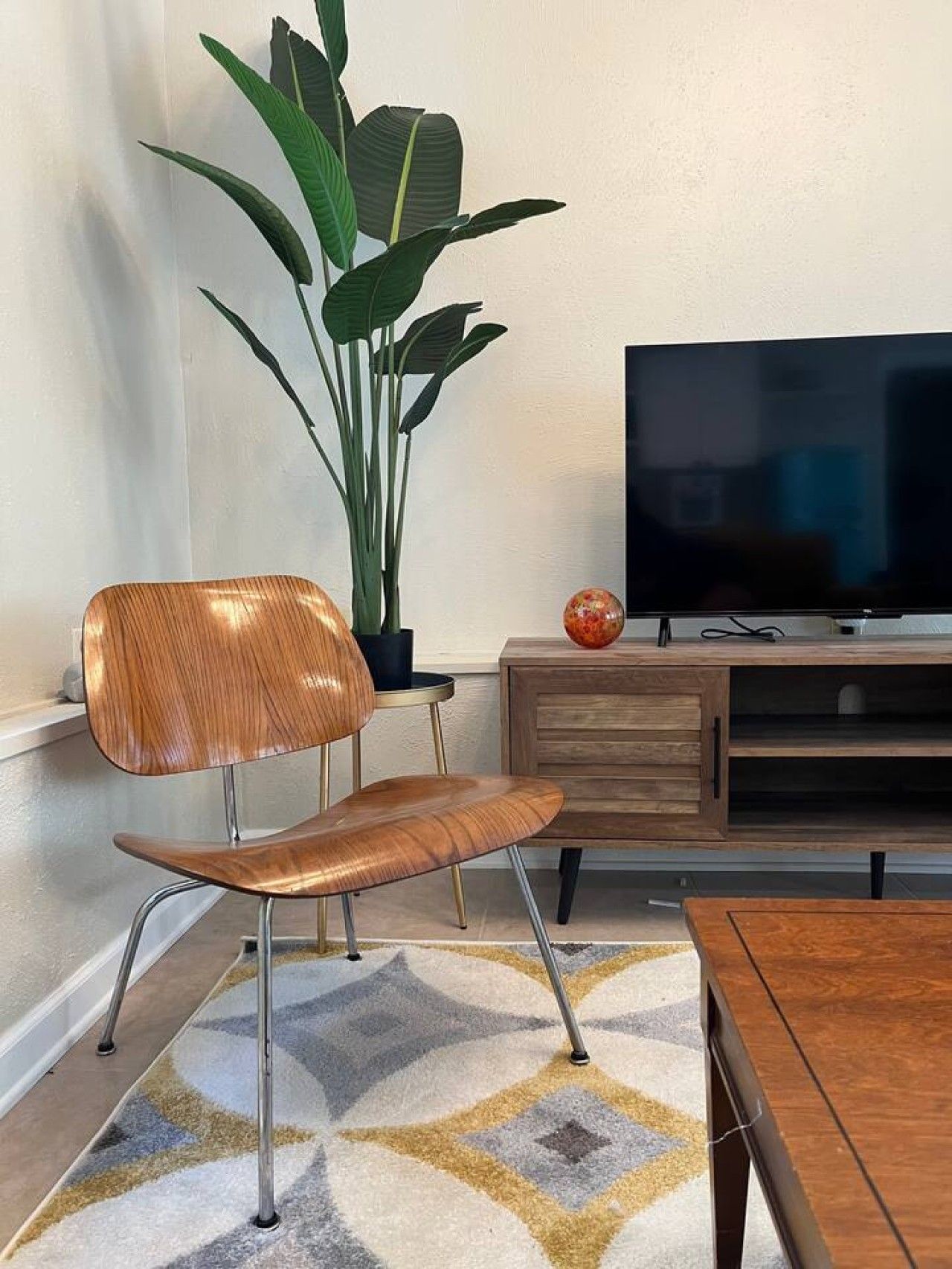 A modern living room with a wooden chair, a television, a plant, and a decorative globe.