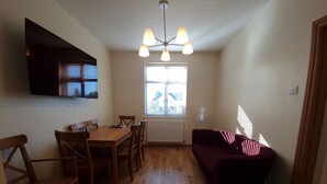 En kompakt bolig med et træspisebord, stole, en sofa og en loftlampe.