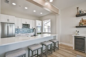 A modern kitchen with white cabinetry, a large island with bar stools, and built-in appliances.