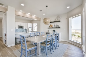 A modern kitchen with white cabinets, a central island, and a dining area with blue chairs and a wooden table.
