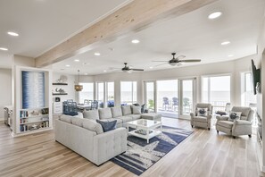 A spacious living room with a large sectional sofa, a coffee table, and a fireplace. There are multiple ceiling fans and large windows providing natural light. - Luxurious Beach Front vacation home perfect for large groups, with elevator. (Galveston)