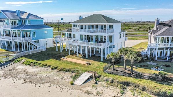 A coastal residential area with multiple beachfront houses featuring balconies, large windows, and a sandy beach in the foreground.