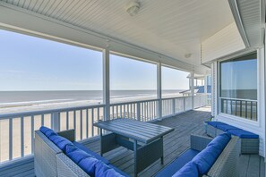Een overdekt terras met uitzicht op het strand, met een tafel en zithoek.