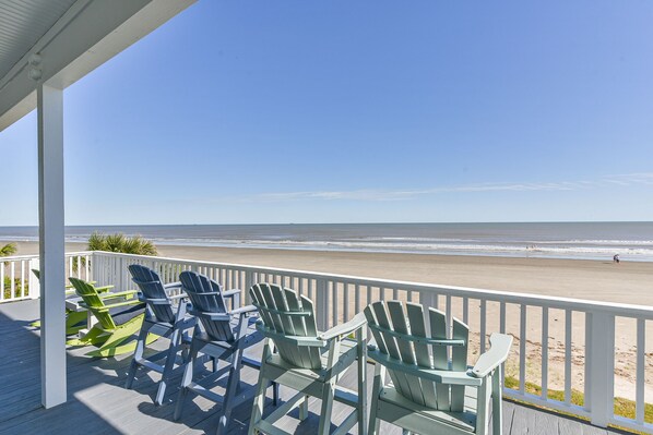Uitzicht op het strand vanaf een overdekt terras met Adirondack-stoelen.