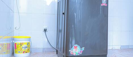 A compact refrigerator with a sticker, a power outlet, and two buckets on a tiled floor.