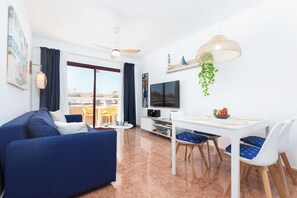 A modern living room with a sofa, TV, dining table, chairs, and a balcony view.