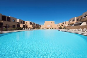 A swimming pool with lounge chairs, a clear blue sky, and buildings in the background.