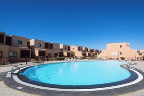 Une piscine entourée de bùtiments modernes, avec un ciel bleu dégagé.