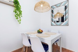 A dining area with a white table, white chairs, a woven pendant light, a mirror with a chevron frame, and a hanging plant.