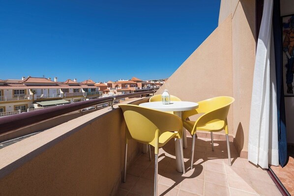 A balcony with yellow chairs and a table, overlooking a residential area.