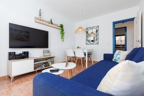 A living room with a TV, white furniture, a blue sofa, and a dining area.
