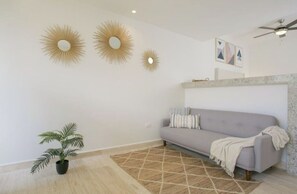 Un salon avec un canapé gris, un tapis à motifs et des appliques murales décoratives.