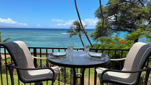 Une table ronde avec deux chaises, un verre d’eau et une assiette, le tout sur un balcon donnant sur l’océan.