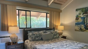 Une chambre à coucher avec un lit, deux lampes de chevet, une fenêtre avec des rideaux, un tableau au mur et une petite armoire.