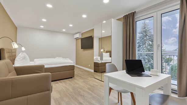 Ett modernt hotellrum med en säng, ett skrivbord med en bärbar dator, en stol och en soffa.