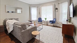 Una sala de estar moderna con un sofá gris, una mesa de centro, un televisor y dos sillas azules.