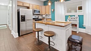 Una cocina moderna con electrodomésticos de acero inoxidable, taburetes de bar de madera y una pared de acento color turquesa.