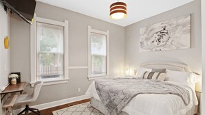 Un dormitorio con una cama, dos ventanas, un escritorio y una silla.