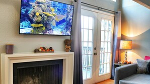 Een woonkamer met een open haard, een televisie erboven en een bank.