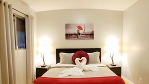 Een hotelkamer met een groot bed, twee nachtkastjes met lampen, een schilderij van de Eiffeltoren, en een rode deken.