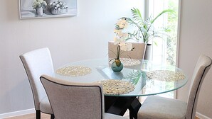 Een eetruimte met een glazen tafel, vier stoelen, een hanglamp en een potplant.