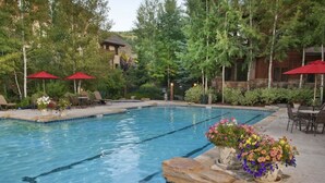 A swimming pool with clear blue water, surrounded by lounge chairs and red umbrellas. - Gorgeous Ski-In Ski-Out Condo on Beaver Creek Mountain (Beaver Creek)