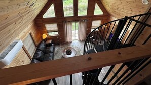 A wooden cabin interior with a loft bedroom, a black leather sofa, a small round table, and a staircase. - Rustic Elegance, 1 bedroom cabin in the heart of Jonesborough. (Jonesborough)