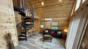 A wooden interior with a spiral staircase, a living area with a sofa and coffee table, and a small rug. - Rustic Elegance, 1 bedroom cabin in the heart of Jonesborough. (Jonesborough)