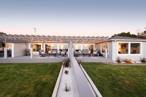 Et moderne hus med en overdækket terrasse, udendørs møbler og en velplejet græsplæne.
