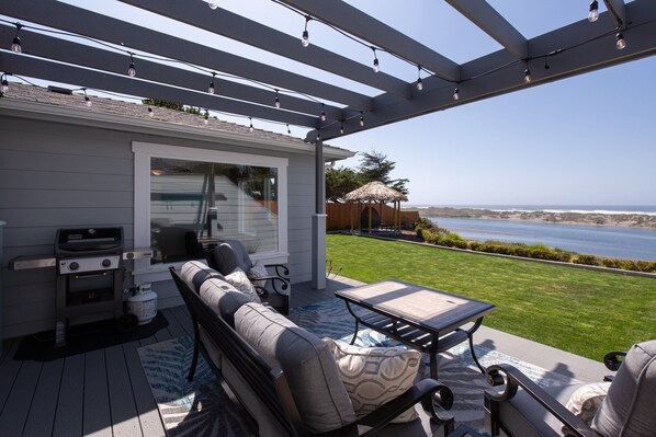 A covered patio with a grill, seating area, and a view of the ocean.
