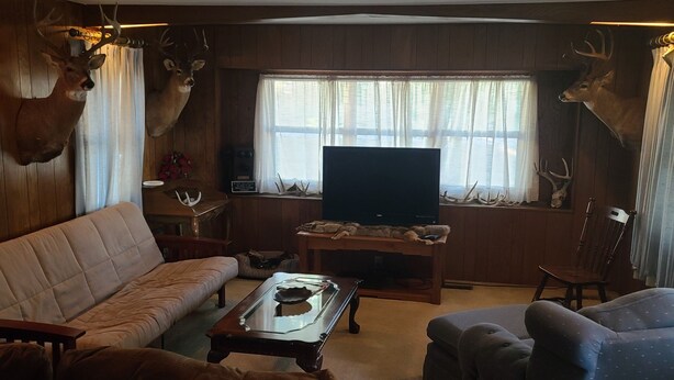 A cozy living room with a sofa, armchairs, a coffee table, and a television. Deer antlers are mounted on the walls.