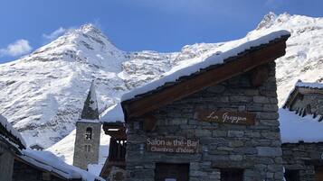 Un bâtiment en pierre sur lequel est apposée une enseigne indiquant « Salon de thé - Bar - Chambres d'hôtes », situé dans une région montagneuse enneigée.