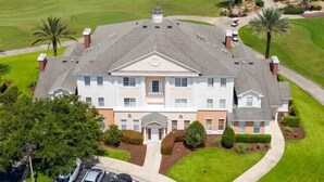 A large, two-story building with a symmetrical facade, surrounded by a well-maintained lawn and palm trees. - Amazing Golf View Condo Best view in Reunion! (Kissimmee)