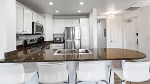 A modern kitchen with white cabinets, stainless steel appliances, and a central island with four white chairs. - Amazing Golf View Condo Best view in Reunion! (Kissimmee)