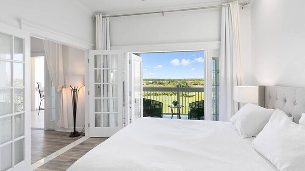 A spacious bedroom with a large bed, a ceiling fan, and a balcony with a view of the landscape. - Amazing Golf View Condo Best view in Reunion! (Kissimmee)