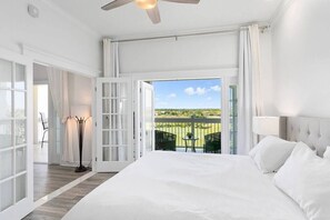 Une chambre spacieuse avec un grand lit, un ventilateur de plafond et un balcon offrant une vue sur le paysage.