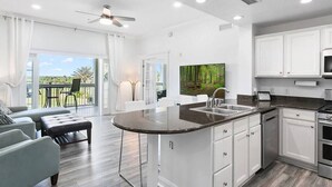 A modern kitchen with white cabinets, a granite countertop, and a large window overlooking a garden. - Amazing Golf View Condo Best view in Reunion! (Kissimmee)