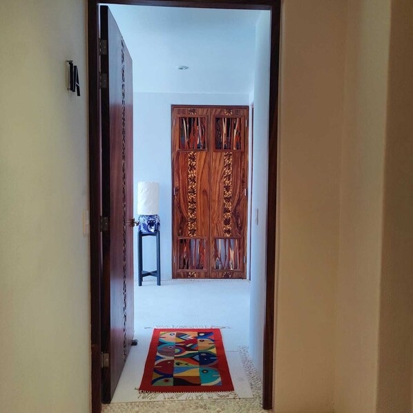 Un pasillo con una puerta de madera, un taburete pequeño y una alfombra colorida.