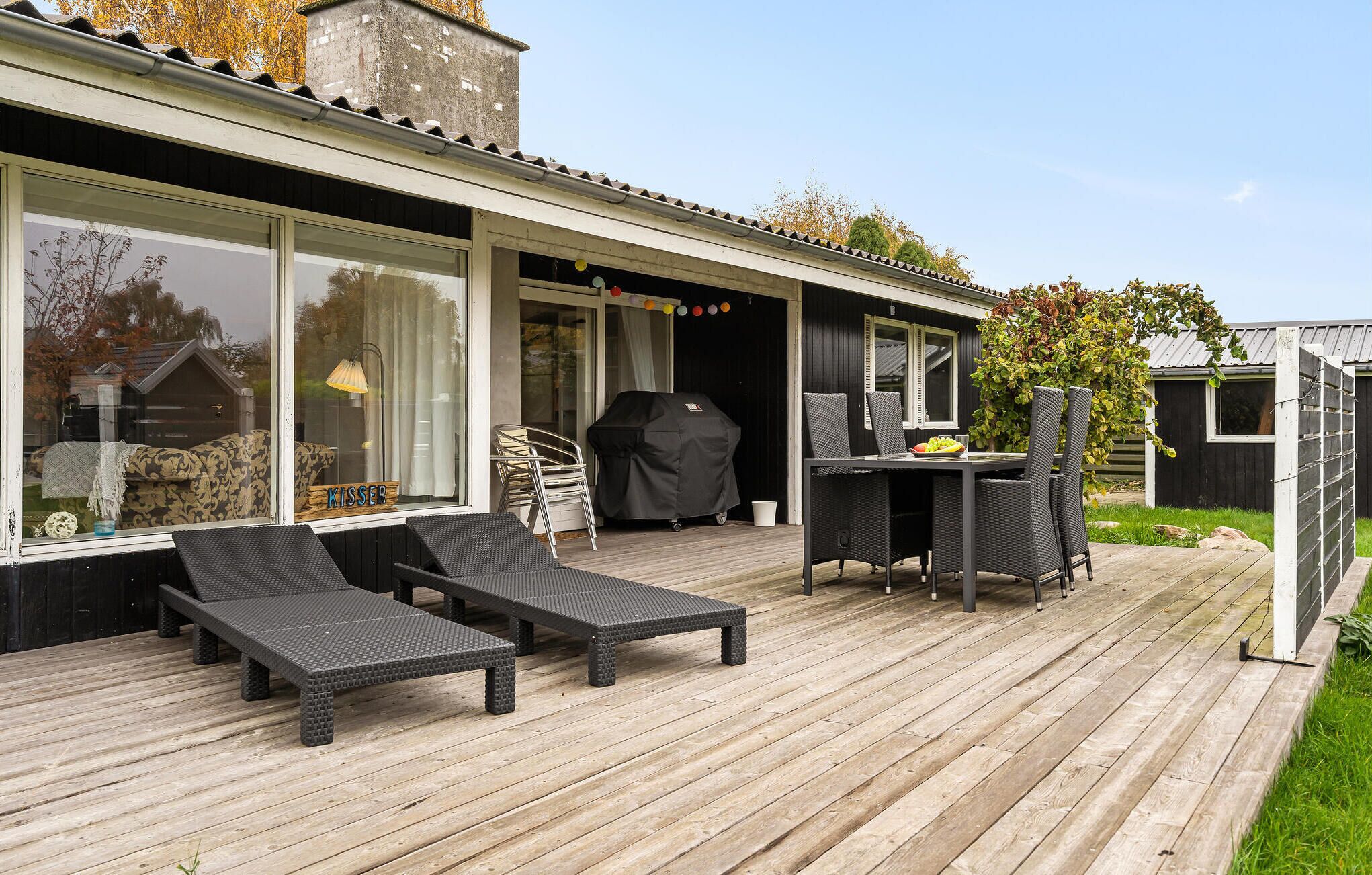 A wooden deck with outdoor furniture, a grill, and a dining area with chairs and a table.