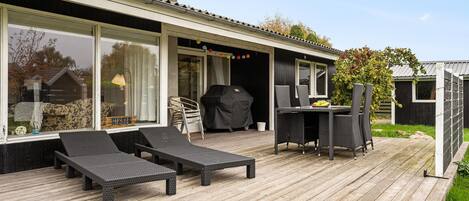 A wooden deck with outdoor furniture, a grill, and a dining area with chairs and a table.