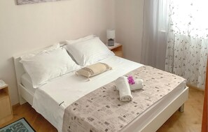 A neatly made bed with white linens, a patterned bedspread, and a rolled towel with a purple flower.