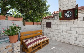 A wooden bench with a striped cushion, a dartboard, and potted plants against a stone wall.